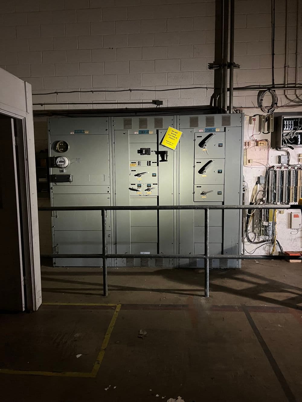 Industrial electrical control panel in a dimly lit room with warning sign.